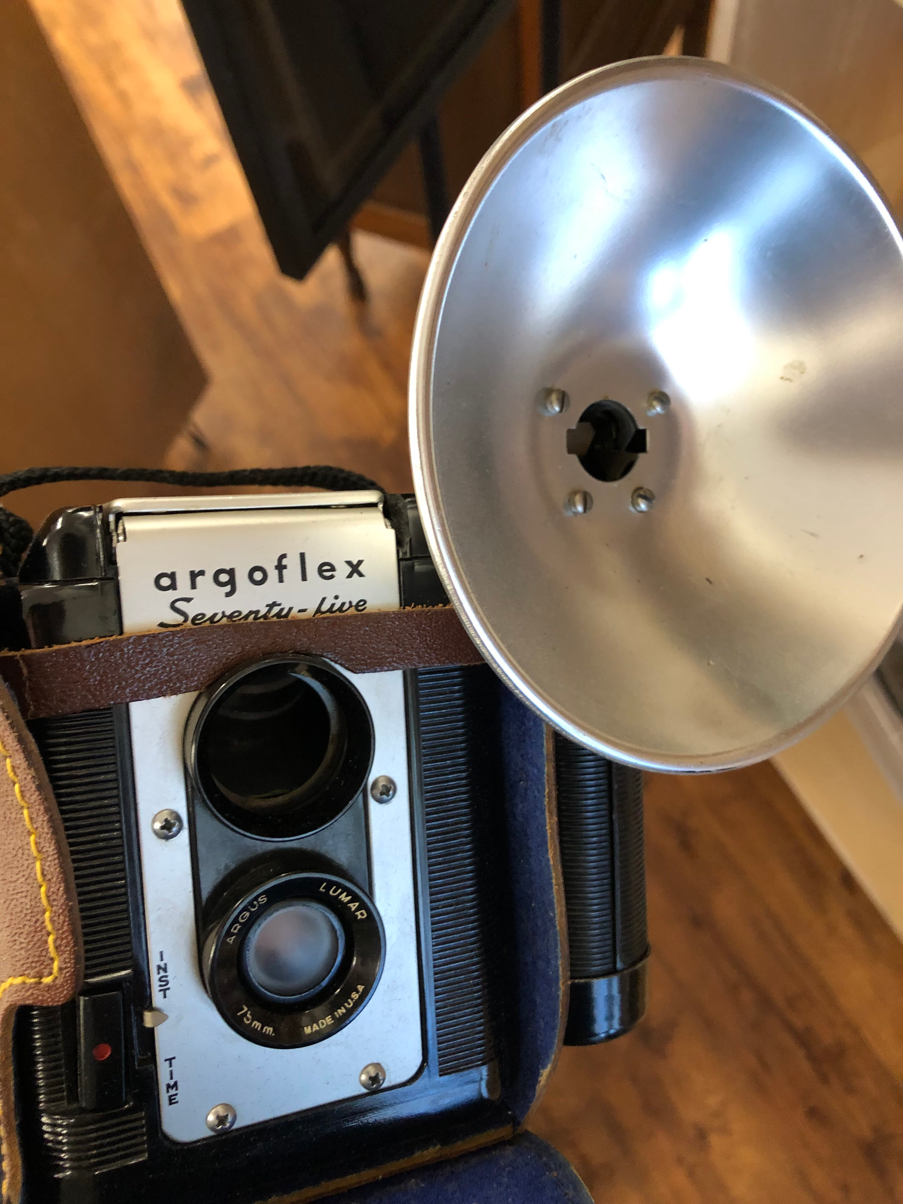 a black and silver two lens camera with a large flash attachment on one side in a brown leather case