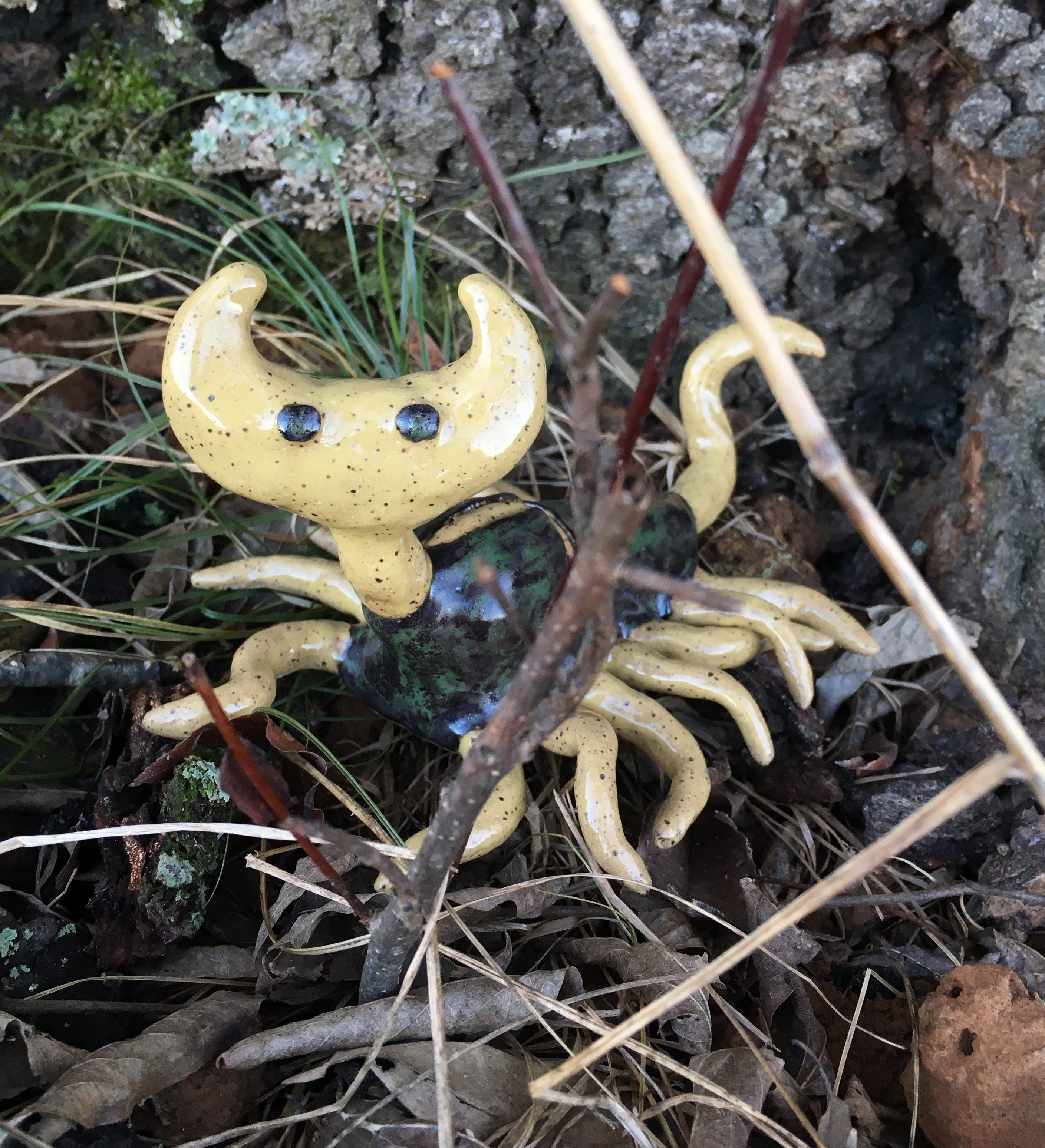 photo of a ceramic wayne larva from the game ‘hylics 2.’ it sits in a nest of leaves and sticks at the foot of a tree, facing the camera